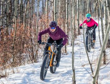 two people mountain biking in winter along snowy trail