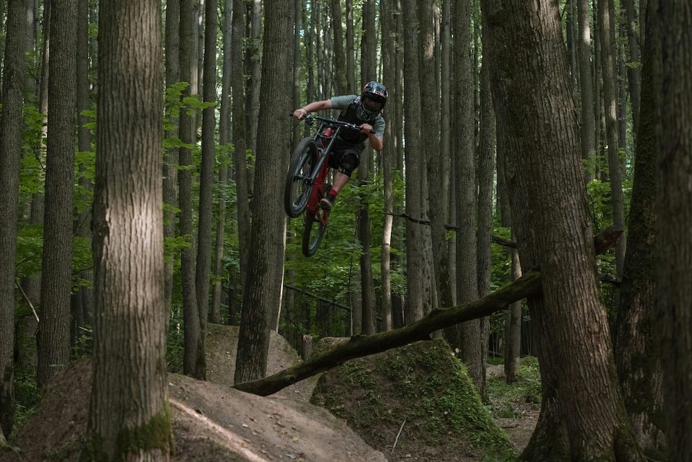 person making massive jump on mountain bike in woods